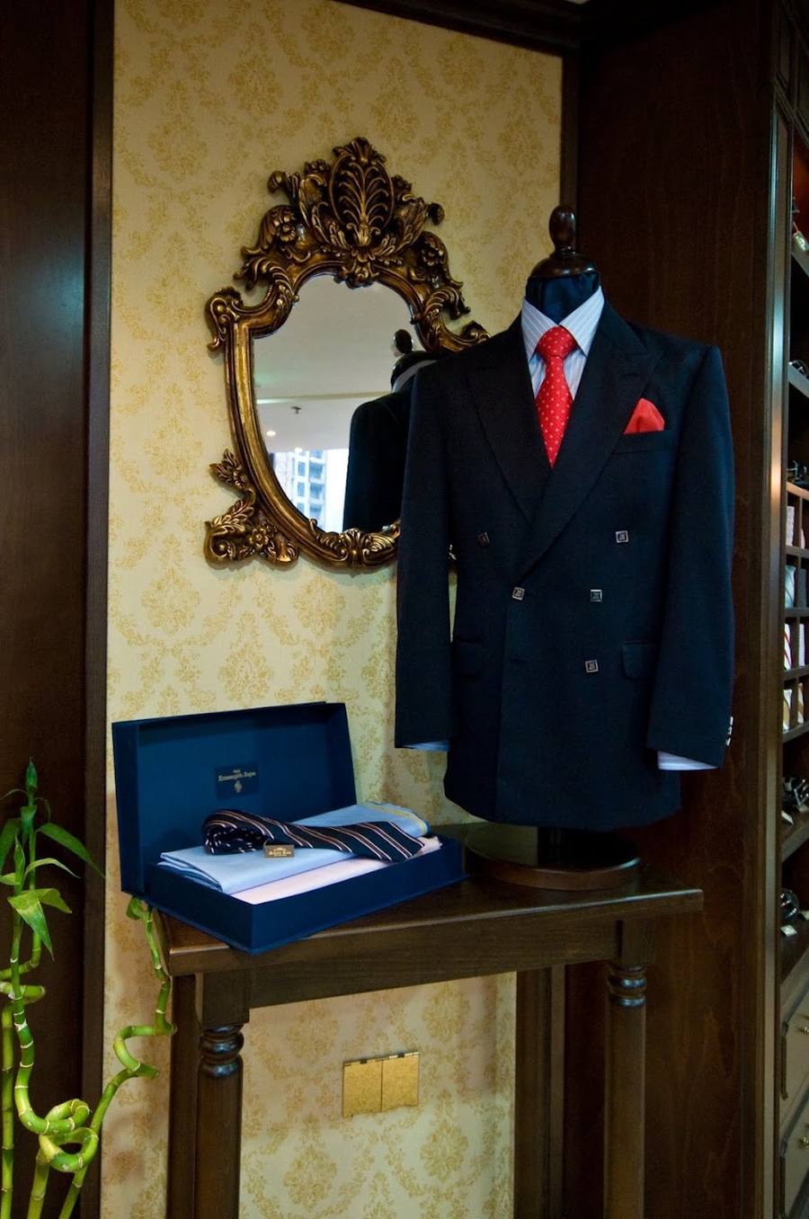 A navy bespoke suit on a stand beside a gilded mirror